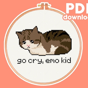 May include: A cross-stitch pattern featuring a brown and white cat with a sad expression, lying on its side. The text "go cry, emo kid" is below the cat.