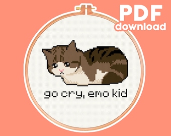 May include: A cross-stitch pattern featuring a brown and white cat with a sad expression, lying on its side. The text "go cry, emo kid" is below the cat.