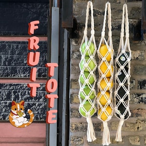 May include: Three macrame hanging fruit totes with a variety of fruits including limes, lemons, and avocados. The totes are made with natural cream-colored cord and are hanging from a brick wall. The text "FRUIT TOTE" is visible on the left side of the image.