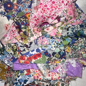 May include: A collection of fabric scraps in various floral patterns, including pink, blue, and green. The fabrics are arranged in a layered, overlapping pattern, creating a textured and colorful background.