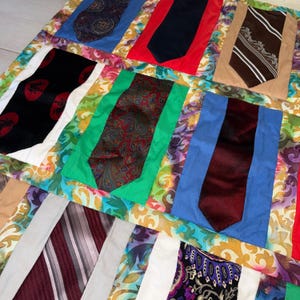 May include: A patchwork quilt featuring a variety of neckties in different colors and patterns. The ties are set against colorful fabric squares, creating a vibrant and textured design. The quilt showcases a mix of paisley, striped, and solid-colored ties.