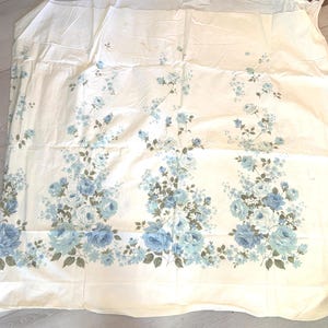 May include: Cream-colored fabric with a floral pattern featuring blue roses and smaller blue and white flowers. The floral design is concentrated along the bottom edge of the fabric, with scattered floral accents across the top.
