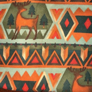 May include: A patterned fabric featuring a repeating design of orange deer, green pine trees, and geometric shapes in orange, red, and teal. The design has a rustic, outdoorsy theme, with a soft, textured appearance.