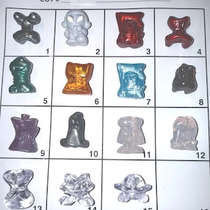 May include: A collection of sixteen small, colorful, and uniquely shaped figurines, each in a different color and design. The figurines are arranged in a grid pattern on a white background, with the text "LOT # 111" at the top.