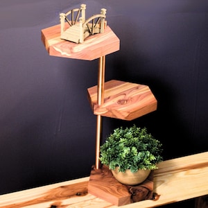 May include: A wooden hexagonal tiered stand with a gold metal pole. The stand has three tiers and is decorated with a small gold bridge on the top tier. A small potted plant sits on the bottom tier.