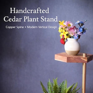 May include: Handcrafted cedar plant stand with a copper spine and modern vertical design. The stand features three cedar shelves and holds a white vase with colorful flowers and a potted fern. The stand is on a wooden surface.