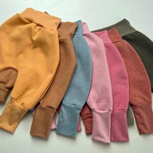 Könnte beinhalten: Sieben Baby-Haremshosen in verschiedenen Farben, darunter Senfgelb, Braun, Blau, Rosa und Olivgrün. Die Hosen haben einen hohen Bund und gerippte Knöchel, aus weichem Stoff.