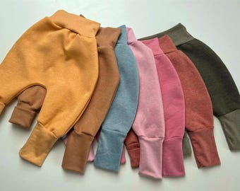 Puede incluir: Colección de siete pantalones de bebé estilo harén en varios colores, incluyendo amarillo mostaza, marrón, azul, rosa y verde oliva. Los pantalones tienen cintura alta y puños, hechos de tela suave.