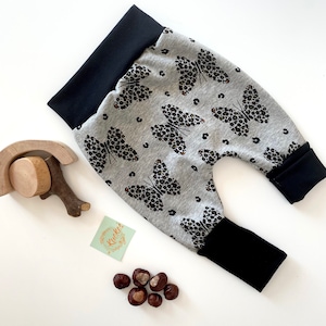 Könnte beinhalten: Graue und schwarze Baby-Leggings mit einem Schmetterlingsmuster. Die Leggings haben schwarze Bündchen und einen schwarzen Bund.