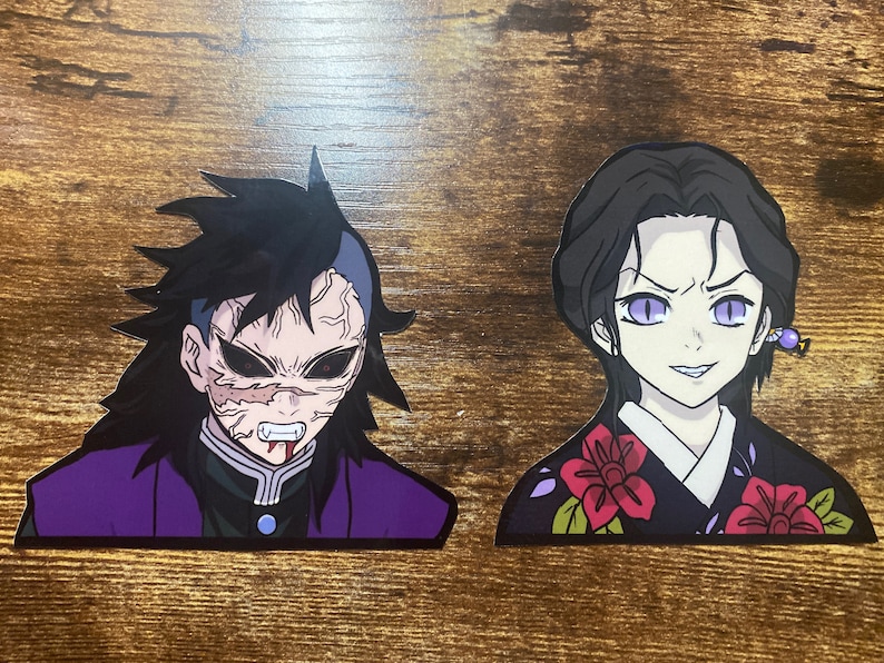 May include: Two anime character stickers, one with a purple and black outfit and the other with a black and red outfit. The character with the purple and black outfit has a menacing expression with sharp teeth and red eyes. The character with the black and red outfit has a more sinister expression with purple eyes.