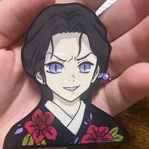 May include: A sticker of a female anime character with black hair, purple eyes, and a smirk. She is wearing a black and purple kimono with red flowers. The sticker is on a hand.