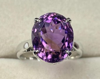 May include: A silver ring with a large, oval-shaped amethyst gemstone. The amethyst is a deep purple color and has a faceted cut.