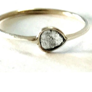 May include: A simple gold band ring with a pear-shaped clear stone set in the centre.