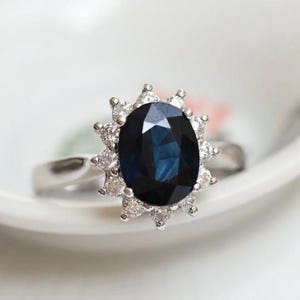Könnte beinhalten: Ein silberner Ring mit einem großen ovalen blauen Saphir, der von kleineren Diamanten umgeben ist.