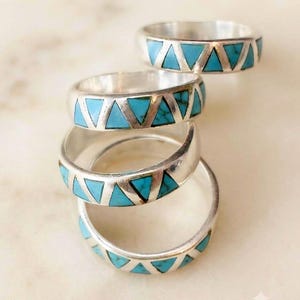 May include: A stack of four silver rings, each featuring a repeating pattern of inlaid triangular turquoise stones. The metal bands are polished and smooth, with the vibrant blue-green stone triangles set evenly around the circumference of each ring.