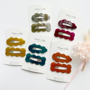 Op de afbeelding: Set van zes haarclips in verschillende kleuren, waaronder teal, groen, bordeauxrood, oranje en geel. De clips zijn wolkvormig en hebben een glanzende afwerking. De verpakking bevat de merknaam "Mango Jelly Accessories" en website-informatie.
