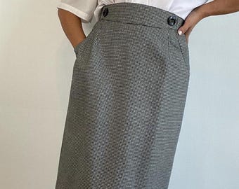 May include: A white short-sleeved blouse with a Peter Pan collar paired with a gray and white houndstooth print pencil skirt. The skirt has two black buttons and a pocket on the left side.