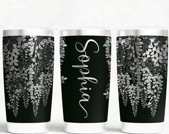 May include: Three black tumblers with white floral designs and the name "Sophia" in cursive. The floral design is silver and white, with a white base and silver rim. The tumblers are cylindrical.