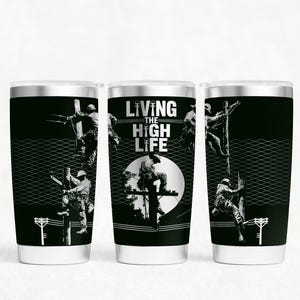 Könnte beinhalten: Drei schwarze isolierte Becher mit silbernem Rand. Jeder Becher zeigt eine schwarz-weiße Grafik eines Monteurs, der einen Strommast erklimmt. Der Text "LIVING THE HIGH LIFE" ist auf dem mittleren Becher zu sehen.