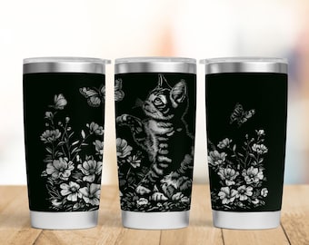 Puede incluir: Tres vasos térmicos negros con un diseño de gato y mariposa. El gato está en un campo de flores, extendiendo la pata hacia una mariposa. El diseño es blanco sobre fondo negro. Los vasos tienen tapas plateadas y bases blancas.