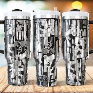 Könnte beinhalten: Drei Edelstahl-Reisebecher mit schwarzen Griffen und weißen Deckeln. Die Becher sind mit einem schwarz-weißen Muster aus verschiedenen Schusswaffen und Kugeln bedeckt. Die Becher stehen auf einer Holzoberfläche.