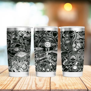 Könnte beinhalten: Drei Edelstahlbecher mit einem schwarz-weißen Grafikdruck von Auto-Motorteilen. Die Becher stehen auf einer Holzoberfläche.