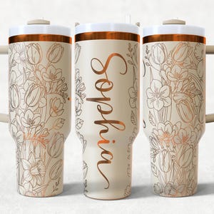 May include: A cream-coloured tumbler with a floral design in copper tones. The tumbler features the name "Sophia" in a copper script font. The lid and handle are a neutral colour, and the rim is copper.