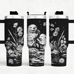 May include: Black and white graphic of two otters on a black background with white flowers and stars. The graphic is on a stainless steel tumbler with a black lid.