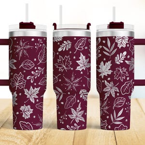 May include: A stainless steel tumbler with a burgundy base and a silver leaf pattern. The tumbler has a lid with a straw hole and a handle.
