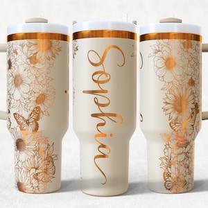 May include: A cream-coloured tumbler with a white lid and a gold band. The tumbler features gold floral and butterfly designs. The name "Sophia" is written in gold script on the front.