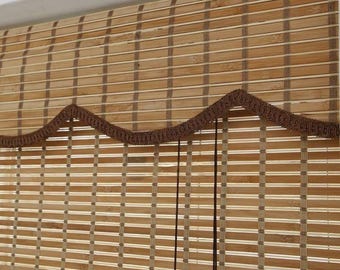 Puede incluir: Persianas de bambú natural tejidas con un ribete festoneado marrón. Las persianas están levantadas, mostrando la textura natural del bambú.