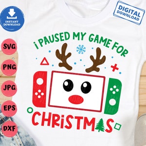 May include: White t-shirt with a Christmas-themed graphic. The design features a game console with reindeer antlers, the text "I PAUSED MY GAME FOR CHRISTMAS," and a snowflake. The shirt also has the words "DIGITAL DOWNLOAD" and file type icons.