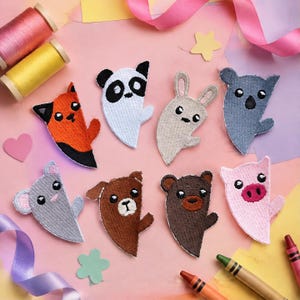Pode incluir: Uma coleção de oito emblemas bordados de animais, incluindo uma raposa, panda, coelho, koala, rato, cão, urso e porco. Cada emblema tem a forma de meio corpo com detalhes costurados, olhos pretos e cores distintas para cada animal.