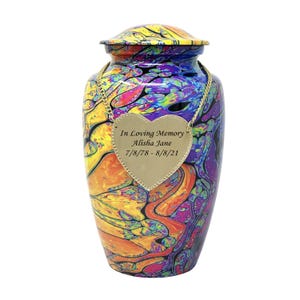 Pu&ograve; includere: Un'urna crematoria colorata con un designo astratto a spirale in tonalit&agrave; di giallo, arancione, rosa, viola e blu. Un'etichetta dorata a forma di cuore &egrave; appesa all'urna con l'iscrizione "In Loving Memory Alisha Jane 7/8/78 - 8/8/21".