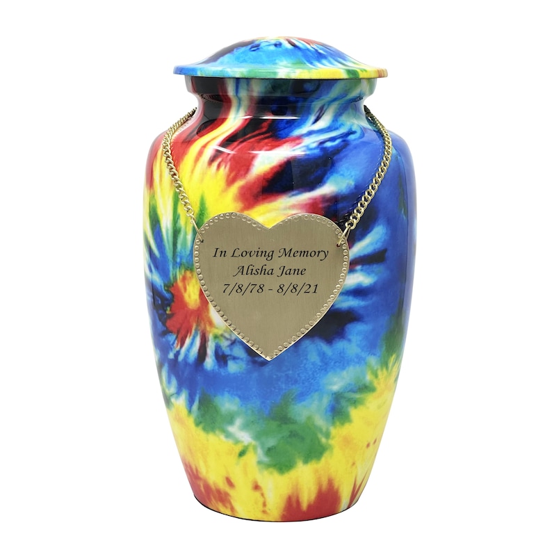 K&ouml;nnte beinhalten: Eine Urne mit einem lebhaften Batikmuster in Blau, Gelb, Rot und Gr&uuml;n. Ein goldfarbener herzf&ouml;rmiger Anh&auml;nger h&auml;ngt an einer Goldkette um den Hals und ist mit dem Text In Loving Memory Alisha Jane 7/8/78 - 8/8/21 graviert.