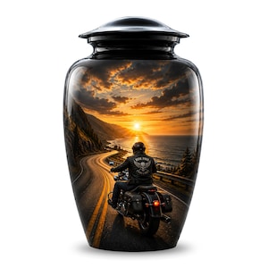 May include: A black metal cremation urn featuring a wrap-around graphic of a motorcyclist riding along a coastal highway at sunset. The rider wears a jacket with a skull and wings emblem and the text RIDE FREE LIVES FOREVER on the back.