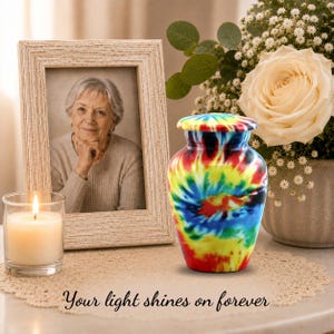 K&ouml;nnte beinhalten: Eine Urne mit einem lebendigen Batikmuster in roten, gelben, blauen und gr&uuml;nen Wirbeln. Die Urne hat einen abgerundeten K&ouml;rper und einen passenden Deckel. Der Text "Your light shines on forever" ist auf der Oberfl&auml;che darunter aufgedruckt.