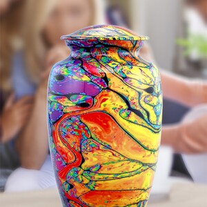 Pu&ograve; includere: Un'urna crematoria colorata con un designo astratto a spirale in tonalit&agrave; di giallo, arancione, rosso, viola e nero.
