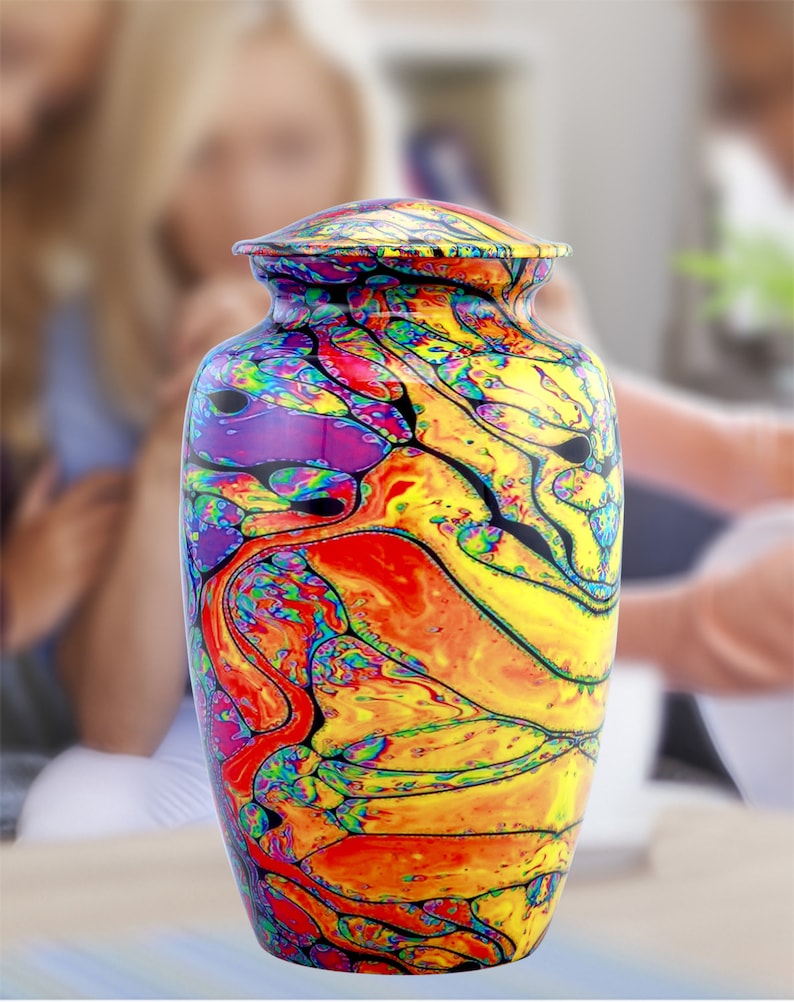 Pu&ograve; includere: Un'urna crematoria colorata con un designo astratto a spirale in tonalit&agrave; di giallo, arancione, rosso, viola e nero.