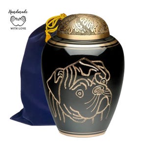 May include: Black cremation urn featuring a gold pug design. The urn has a gold lid with an engraved floral pattern. It comes with a blue velvet bag. Handmade with love.