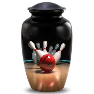 May include: A black, glossy urn with a bowling scene depicted on the front. The image shows white bowling pins with red stripes and a red bowling ball. The urn has a lid and a wooden floor design.