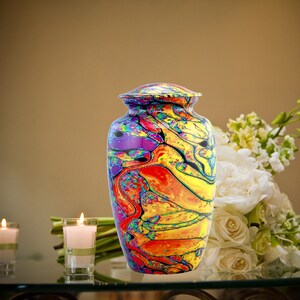 Pu&ograve; includere: Un'urna crematoria colorata con un designo astratto a spirale in tonalit&agrave; di rosso, giallo, blu e viola. L'urna &egrave; realizzata in metallo e ha una finitura lucida.