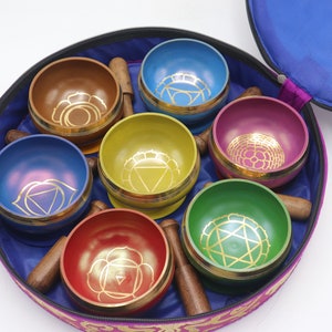 Op de afbeelding: Een set van zeven zangkommen in een ronde draagtas. De kommen zijn in een cirkel gerangschikt en zijn elk van een andere kleur: rood, oranje, geel, groen, blauw, indigo en violet. Elke kom heeft een gouden ontwerp aan de binnenkant. De draagtas is paars met een blauwe voering.