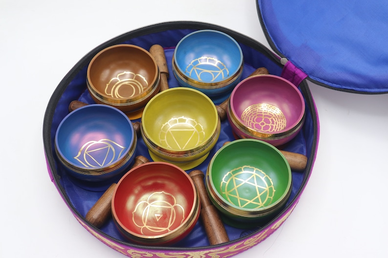 Op de afbeelding: Een set van zeven zangkommen in een ronde draagtas. De kommen zijn in een cirkel gerangschikt en zijn elk van een andere kleur: rood, oranje, geel, groen, blauw, indigo en violet. Elke kom heeft een gouden ontwerp aan de binnenkant. De draagtas is paars met een blauwe voering.