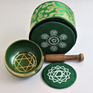 Op de afbeelding: Een groene zangkom met een gouden Davidster-ontwerp, een houten slager en een groen kussen met een wit chakra-symbool. De kom wordt geleverd in een groen-gouden gepatroneerde draagtas.