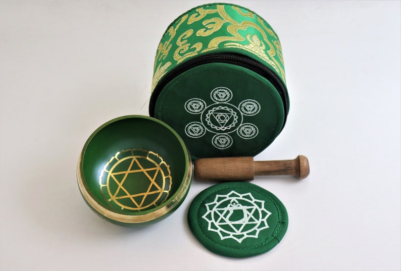 Op de afbeelding: Een groene zangkom met een gouden Davidster-ontwerp, een houten slager en een groen kussen met een wit chakra-symbool. De kom wordt geleverd in een groen-gouden gepatroneerde draagtas.