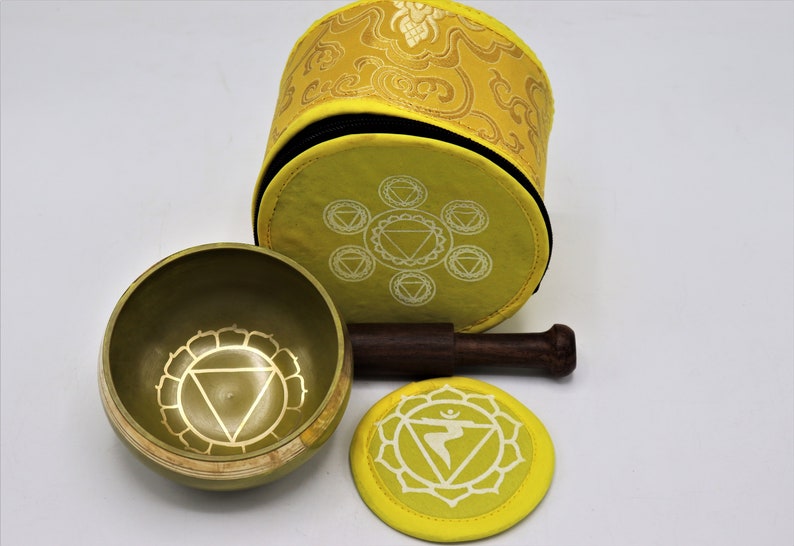 Op de afbeelding: Een gele zangkomset met een houten slaagstok, een geel kussen en een gele draagtas. De kom en het kussen hebben een wit ontwerp van de Manipura chakra, de derde chakra, die geassocieerd wordt met de kleur geel.