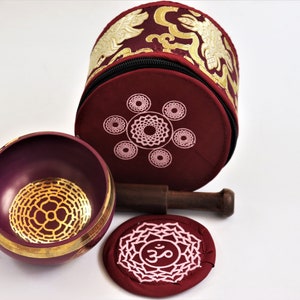 Op de afbeelding: Een bordeauxrode zangkomset met een gouden mandala-ontwerp, een houten slaagstok en een bordeauxrood kussen met een wit Om-symbool.
