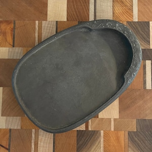 May include: A black ink stone with a carved design around the edge. The stone is oval shaped and has a shallow well in the center.