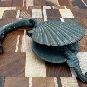May include: A decorative metal door knocker shaped like a seashell with a seahorse tail. The knocker is a dark green colour with a patina finish.